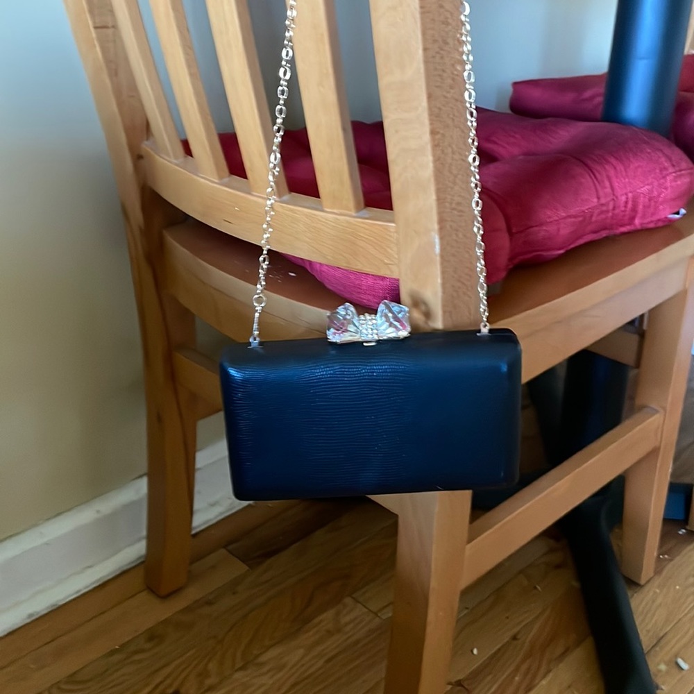 Black clutch with crystal bow shaped buckle. Thin gold strap is removable